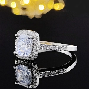 Detail of cushion cut halo engagement ring with pavé diamonds on a reflective base