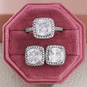 Detailed view of silver ring and earrings set with square halo stones in a pink velvet box