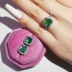 Detailed set of emerald green gemstone ring and stud earrings with halo diamond setting