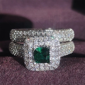 Macro shot of luxury emerald-cut green stone rings with halo diamond setting on velvet