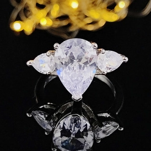 Detailed macro view of silver three-stone ring with pear-cut cubic zirconia on black base