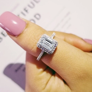 Emerald cut halo ring with pave diamonds on white metal band worn on finger