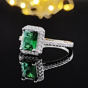 Macro detail of emerald cut green gemstone ring with pavé diamond halo on black mirror