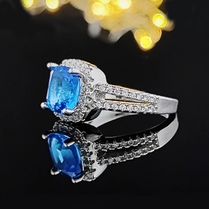 Macro di un anello di lusso con pietra blu quadrata e pavé di diamanti su superficie riflettente