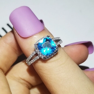 Dettaglio di un anello di lusso con gemma blu quadrata e halo di diamanti sulla mano
