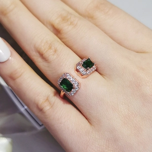 Nahaufnahme eines roségoldenen offenen Rings mit grünen Edelsteinen am Finger