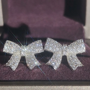 Sparkling silver bow stud earrings with zircon stones on a purple velvet jewelry display