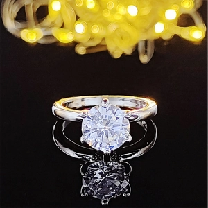 Anillo de diamante de corte redondo con seis garras sobre superficie negra reflectante