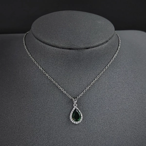 Élégant collier avec pendentif goutte vert émeraude et chaîne argentée sur buste gris