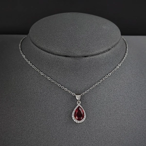 Détail du collier goutte rouge avec accents de diamants blancs sur un buste gris