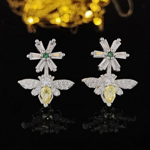 Detalle de pendientes de flor y abeja en plata con circonitas verdes y amarillas