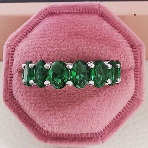 Makro-Detail eines Silberrings mit sieben ovalen grünen Steinen in rosa Samtbox