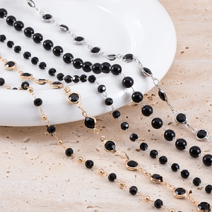 Close-up of gold and silver plated chains with black beads on a ceramic plate
