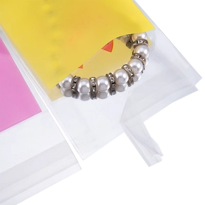Detalle de bolsa joyería transparente autoadhesiva con cartón rosa y pulsera perlas