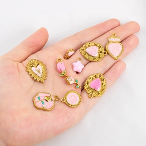 Gros plan de breloques en émail rose fleurs et cœurs pour bijoux DIY dans la main