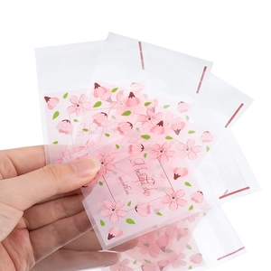Mano che tiene sacchetti regalo traslucidi con fiori di ciliegio e chiusura autoadesiva