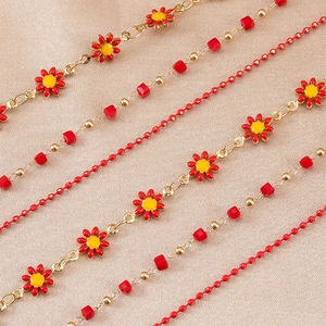 Detail of red enamel daisy pendant with gold chain and beads on champagne satin