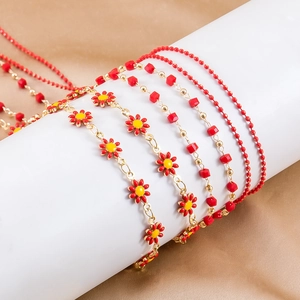 Detail of red enamel daisy bracelet and gold chain with cube beads on a white display