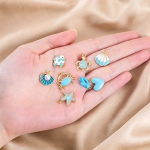 Detail of blue enamel ocean charms including turtle and shell on a palm for DIY jewelry