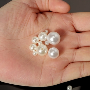 Detailed view of various white faux pearl bead sizes with hole on a hand for scale