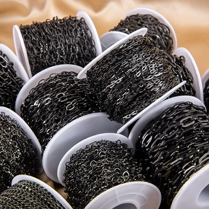 Close-up of bulk black stainless steel heart and star shaped chains on white spools