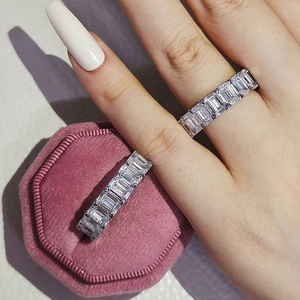 Rectangle cut cubic zirconia eternity band on finger next to pink velvet gift box