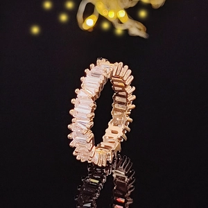 Makrofoto eines Roségold-Ewigkeitsrings mit Zirkonia im Baguetteschliff und goldenem Bokeh