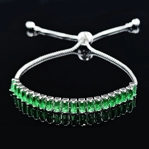 Macro view of adjustable silver bracelet with claw-set emerald-cut green gemstones