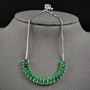 Detail view of silver adjustable bracelet with emerald cut green gemstones in half-arc layout