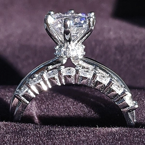 Detail of round cut diamond ring with six-prong setting and pavé accents on purple velvet
