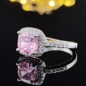 Macro view showing a cushion-cut pink gemstone ring with halo diamonds on a black reflection