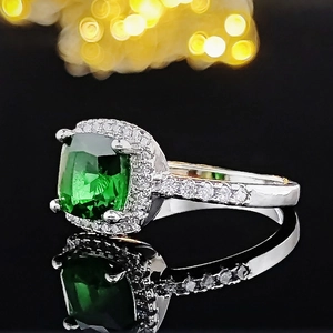 Macro view of emerald cut green gemstone ring with halo diamonds on a reflective background