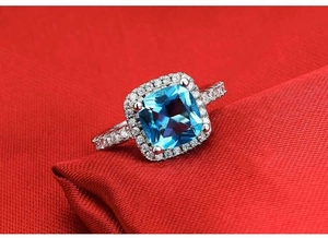 Macro shot of cushion cut blue topaz ring with halo diamond setting on red fabric
