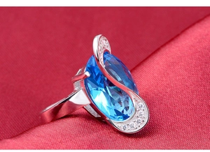 Macro di un anello in argento con una grande gemma blu ovale su seta rossa testurizzata