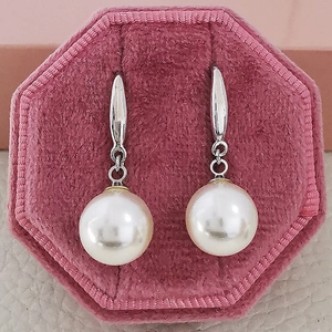 Elegant white round pearl drop earrings with silver hooks on a pink velvet jewelry box