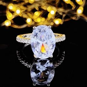 Makroaufnahme eines ovalen Zirkonia-Rings mit Pavé-Band auf einer reflektierenden Basis