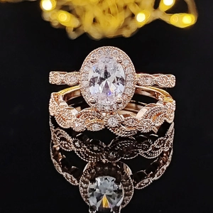 Set di anelli in oro rosa con zircone ovale e fascia a treccia su sfondo nero lucido