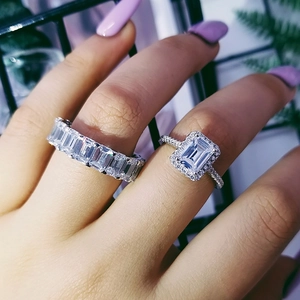 Primer plano de anillos de plata con circonitas talla esmeralda, engaste halo y eternidad