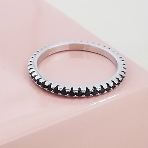 Macro shot of silver eternity ring with black pavé stones on a pink background
