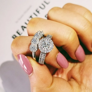 Primer plano de dos anillos de plata S925 con halo y micro-pavé de diamantes en mano