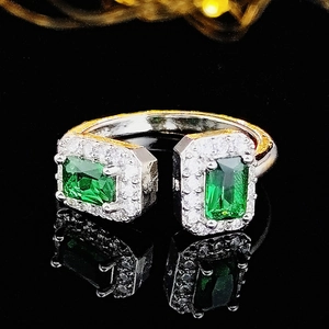 Macro shot of silver ring with dual emerald green stones and diamond accents on black surface