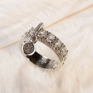 Macro shot of silver wide band ring with round cubic zirconia and dangling pavé charm