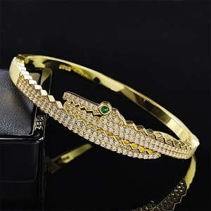 Bracelet doré ouvert avec design zigzag, zircons clairs et accent de pierre verte