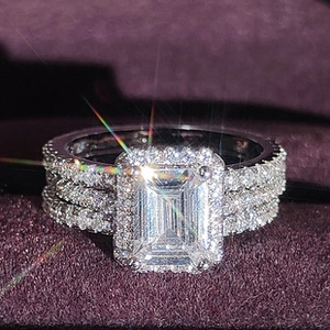Gros plan d'un ensemble de bagues taille émeraude avec halo dans un écrin en velours