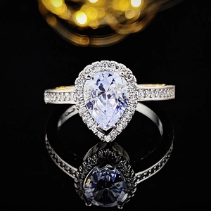 Macro shot of luxury pear-cut halo engagement ring with pavé diamonds on black background