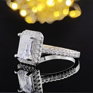 Macro side view of emerald-cut zircon ring with halo setting on a black mirror surface
