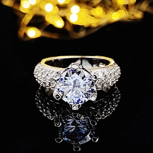 Detalle de un anillo clásico de circonita con seis garras y pavé sobre una base reflectante