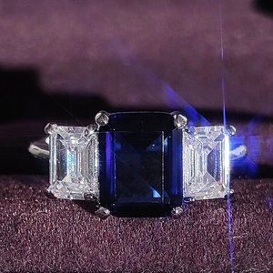 Three-stone ring with emerald-cut blue sapphire and silver band on purple velvet
