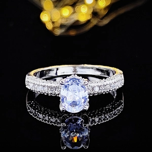 Vista macro de anillo plateado con gema azul ovalada y pavé de diamantes sobre fondo negro