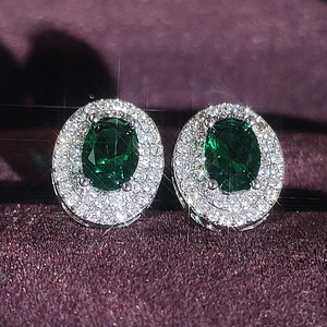 Luxuriöse smaragdgrüne Ohrstecker mit Diamant-Halo auf lila Samthintergrund
